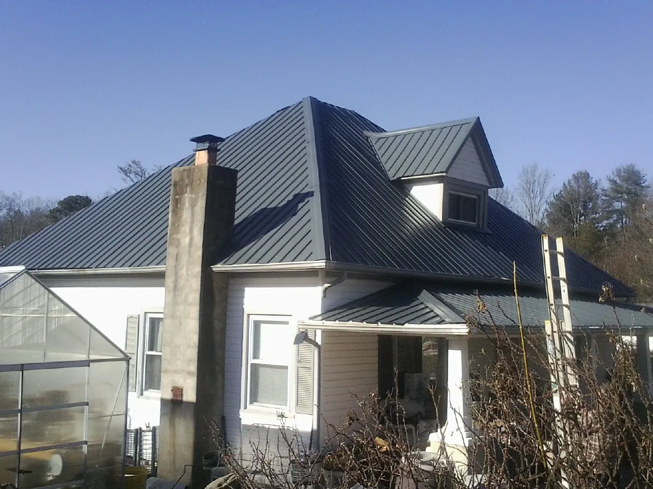 Dark blue standing seam metal roof on a white farmhouse with dormer — Slate & Tile Roof Repair by Roofing Brothers in Grouse Creek