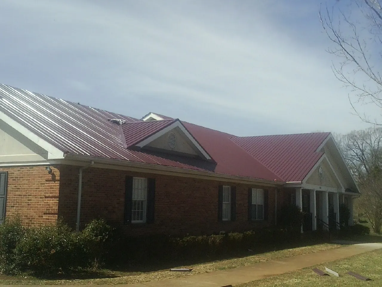 Red metal roof with gabled entries on a long brick building, from a Hail Damage Roof Repair job in Grouse Creek