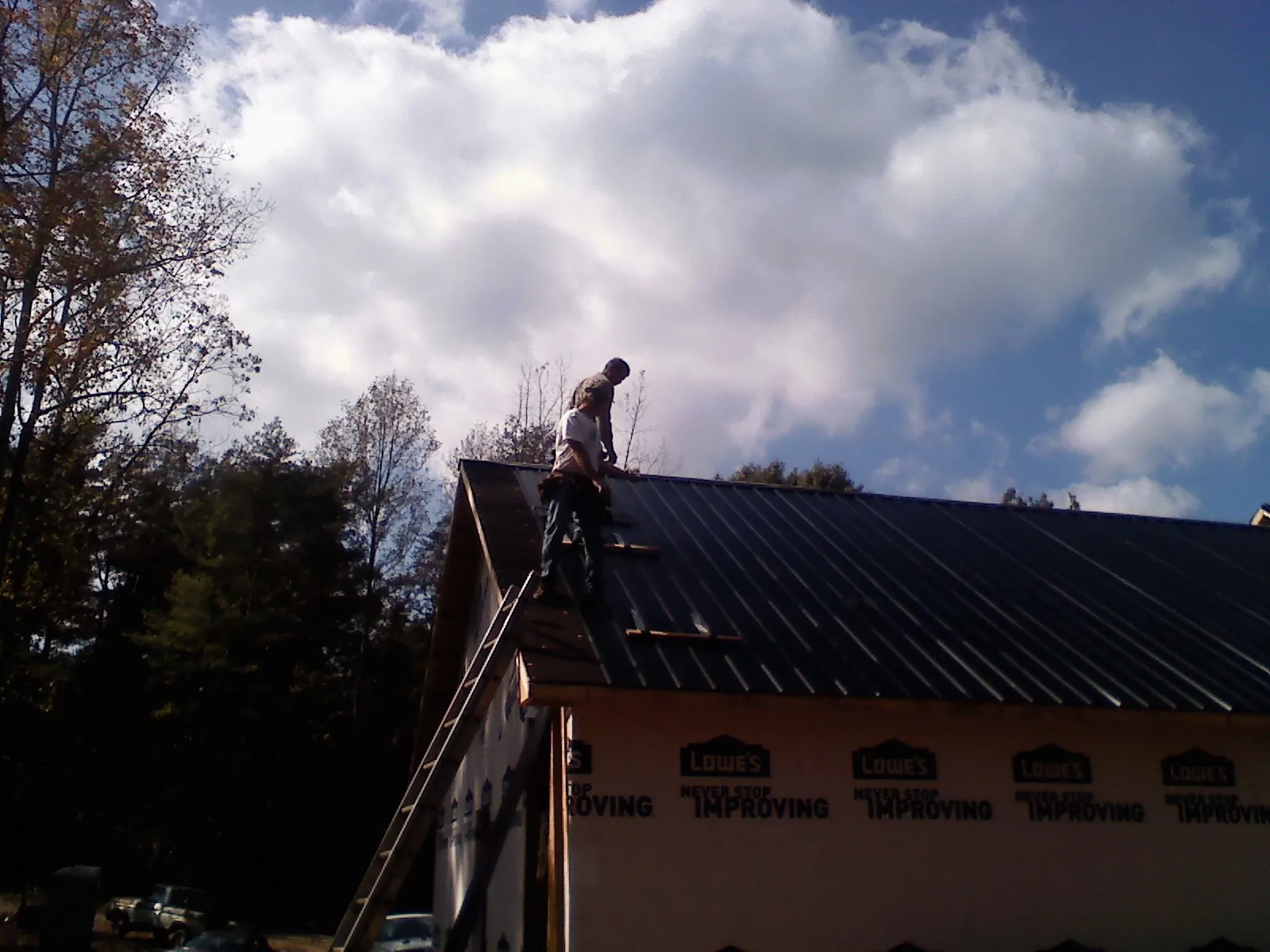 Roofer fastening dark metal panels high against a cloudy sky, from a Roof Inspection job in Grouse Creek