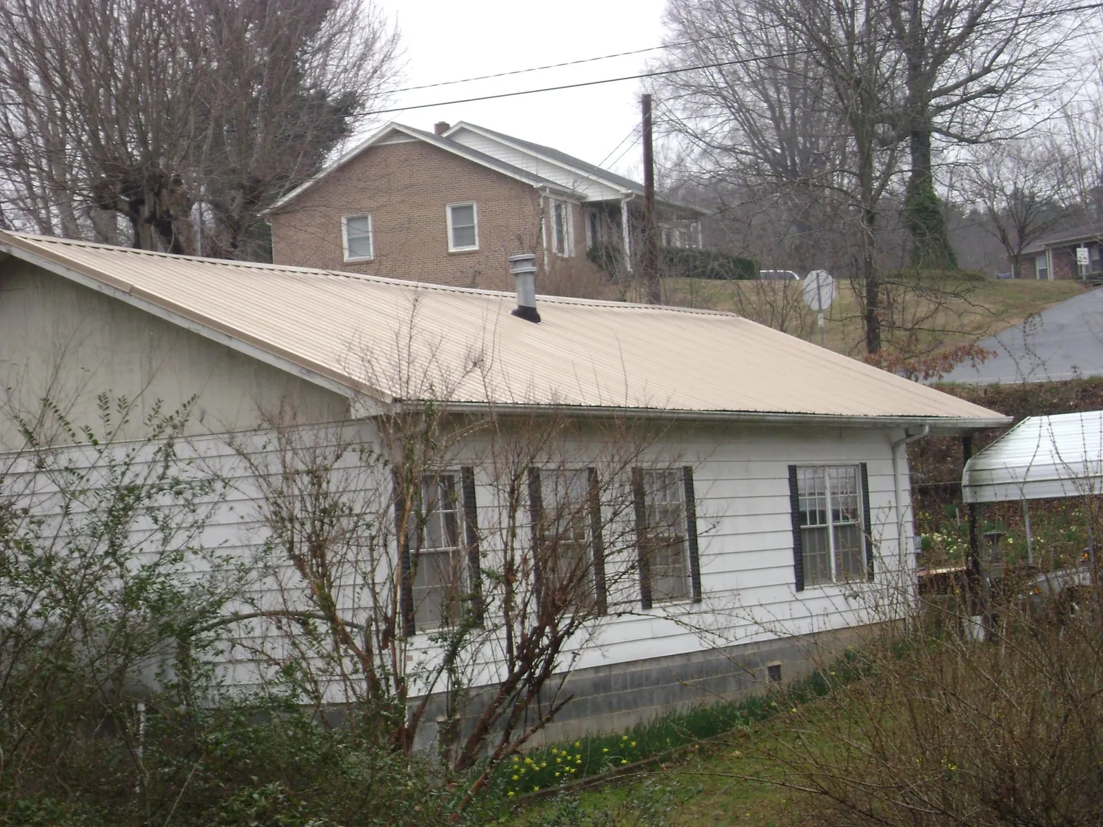 Tan metal roof on a white sided house set into a hillside — Commercial Roofing by Roofing Brothers in Grouse Creek